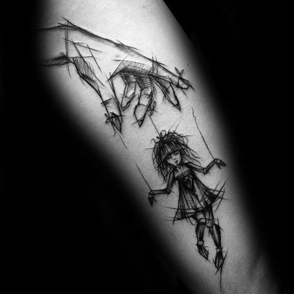 Sketch-style puppet tattoo of a large hand controlling a ragdoll-like girl with messy hair, symbolizing fragility, control, and lost innocence.