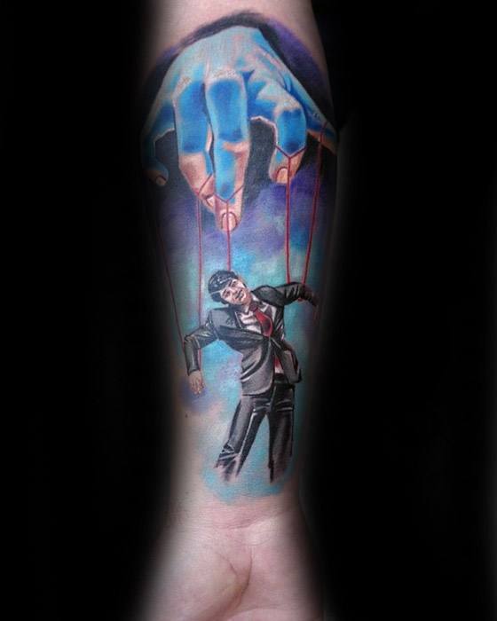 Vibrant puppet tattoo of a blue hand controlling a man in a suit with red strings, symbolizing control, power, or societal pressure.