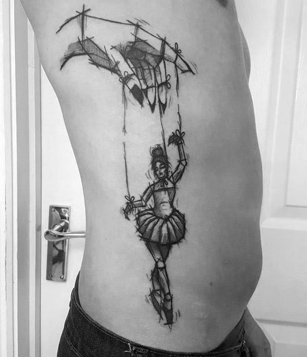 Sketch-style puppet tattoo of a ballerina marionette controlled by a large hand, symbolizing delicate control, grace, and vulnerability.