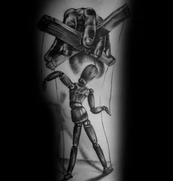 Realistic black and grey puppet tattoo of a wooden mannequin being controlled by a large hand with a crossbar, symbolizing manipulation or lack of free will.