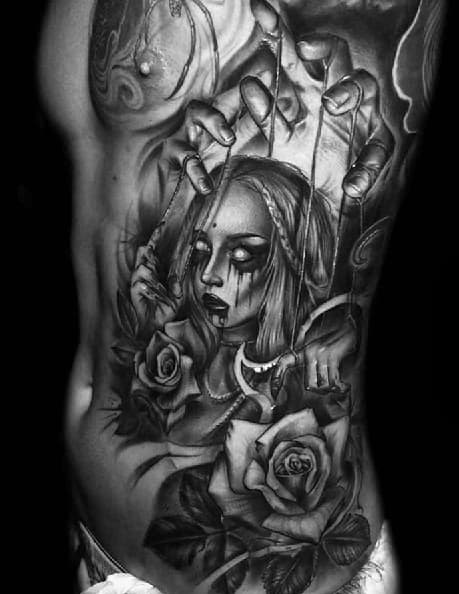 Realistic black and grey puppet tattoo of a sorrowful female marionette with roses, controlled by a hand above, symbolizing beauty, control, and emotional pain.