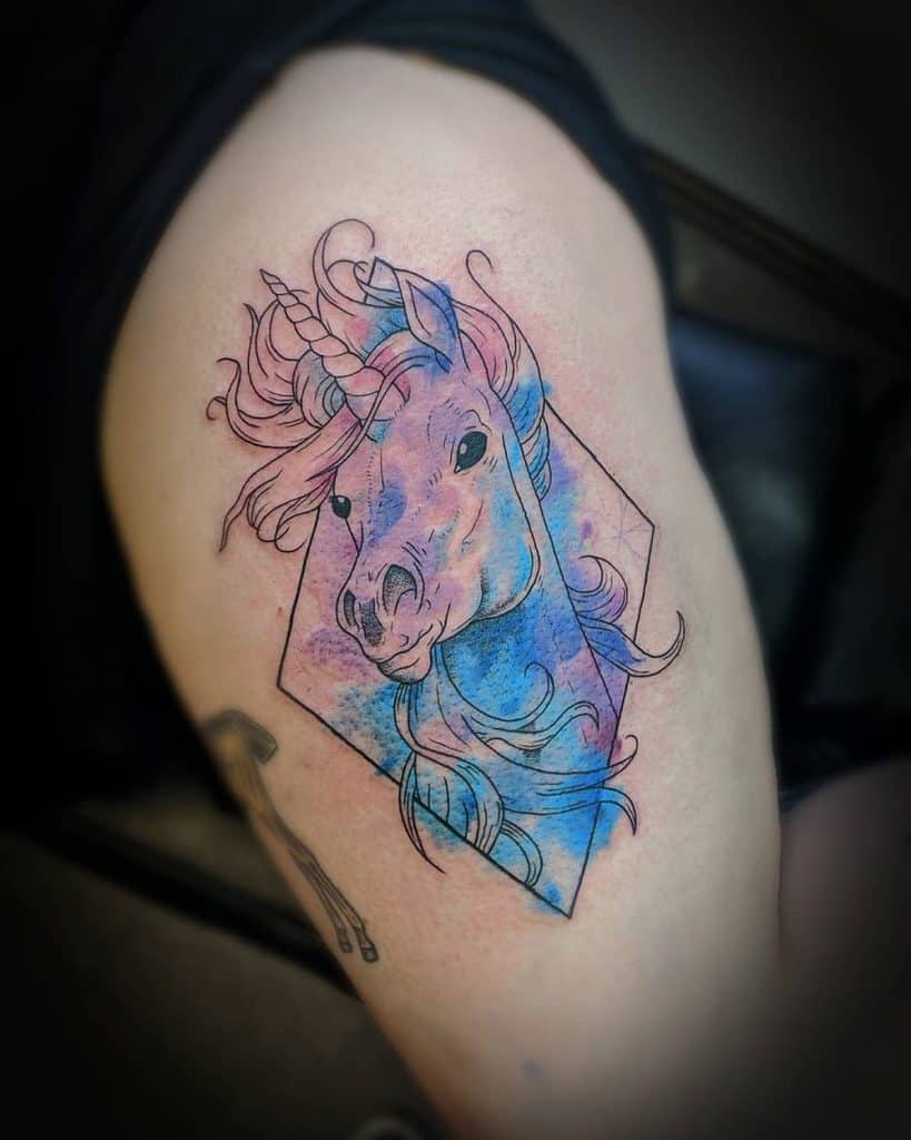 Watercolor-style unicorn tattoo with flowing hair, blending blue and pink hues inside a geometric frame for a dreamy, artistic effect.
