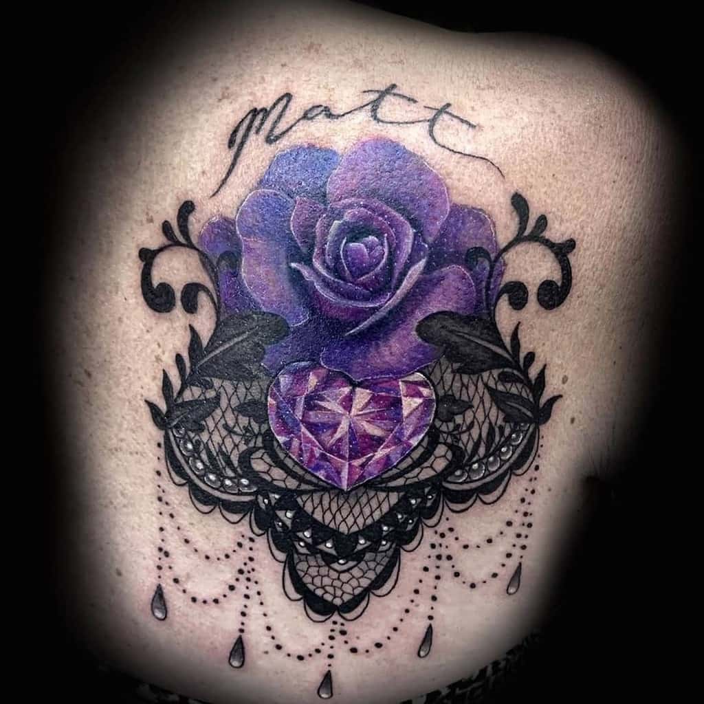 Back tattoo featuring a vibrant purple rose, intricate black lace, a faceted heart-shaped gemstone, and delicate beaded chains, with 'Matt' scripted above.