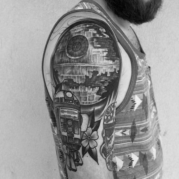 Arm tattoo of the Death Star with a droid in black ink, worn with a patterned tank top