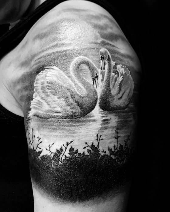 Black and grey tattoo of two swans forming a heart shape with their necks on a reflective lake, framed by silhouetted plants and cloudy skies.