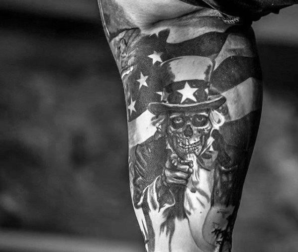 Skull-faced Uncle Sam tattoo in black and gray, pointing forward with a tattered American flag waving in the background.