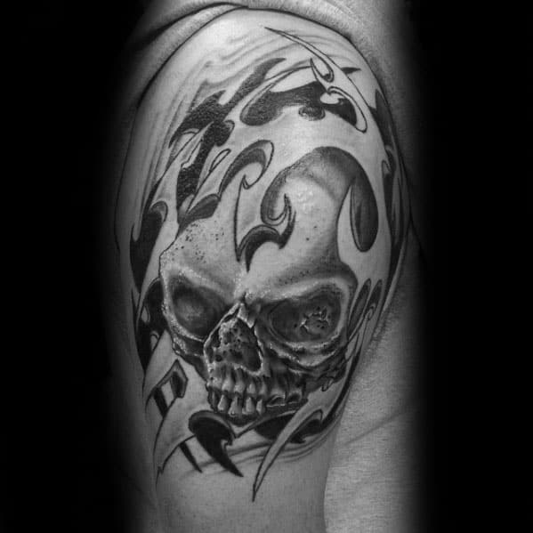 Realistic skull tattoo on upper arm surrounded by abstract tribal flames and dark shading for a bold, intense look.