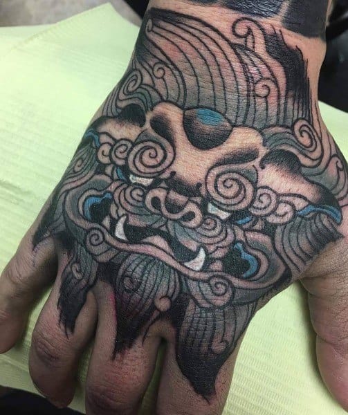 Intricate hand tattoo of a stylized Pandaren guardian from World of Warcraft, featuring bold lines, swirling patterns, and fierce expression.