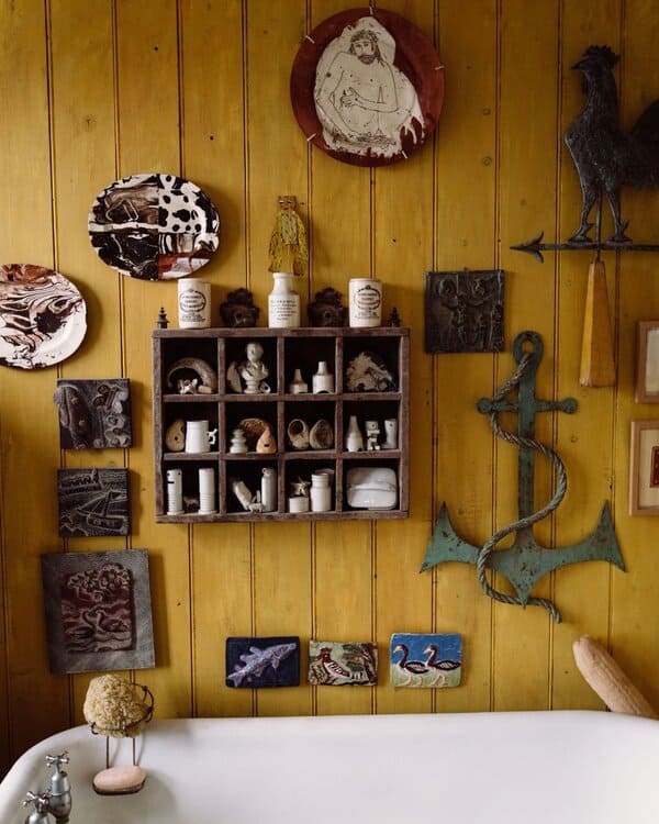 Bathroom featuring rustic yellow wood paneling, eclectic art pieces, a metal anchor, and a simple white tub for a warm, vintage look.