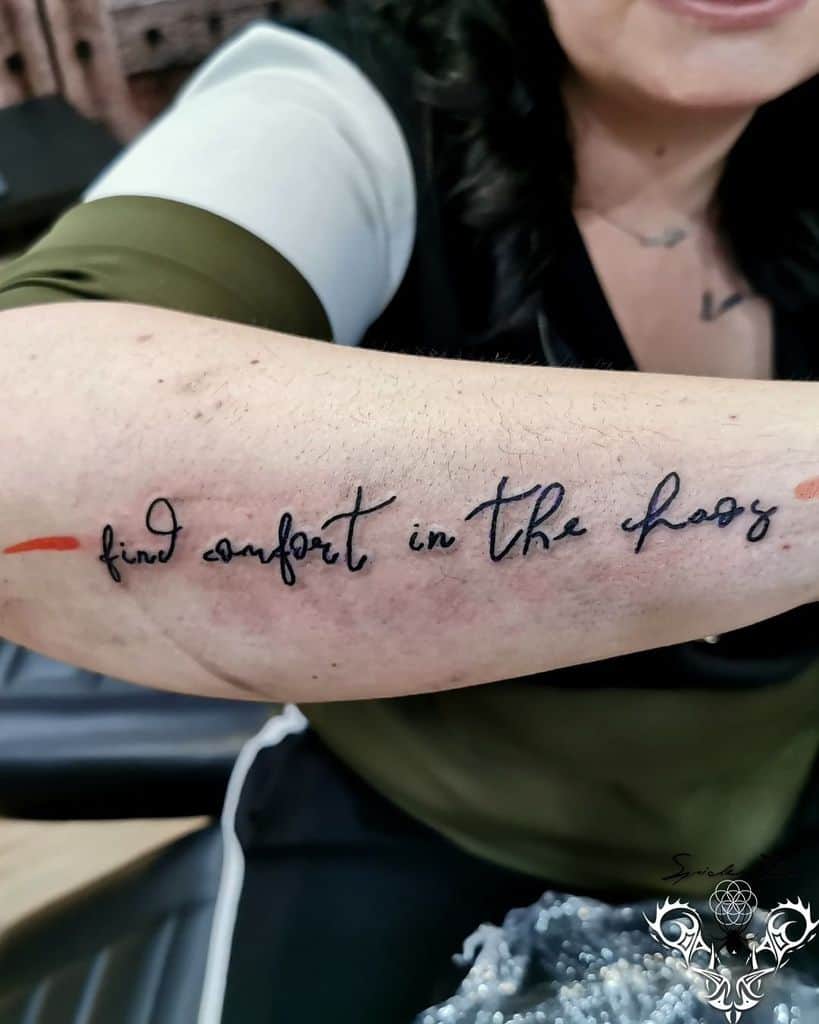 A woman's forearm with a tattoo that reads "find comfort in the chaos" in cursive script