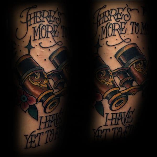 Vintage-style binoculars tattoo with floral details and the phrase 'There's more to me I have yet to find,' symbolizing self-discovery.