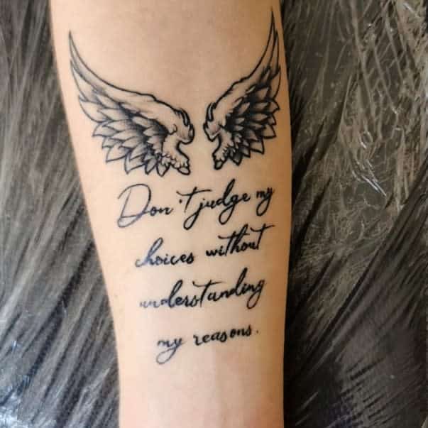 Tattoo of angel wings above the text "Don't judge my choices without understanding my reasons"