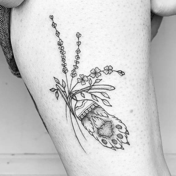 A black and white tattoo of a bouquet with lavender, small flowers, and intricate patterns on the stems, placed on the upper thigh.