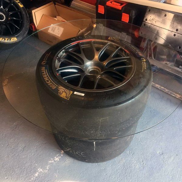 A round glass tabletop resting on a stack of two racing tires in a garage