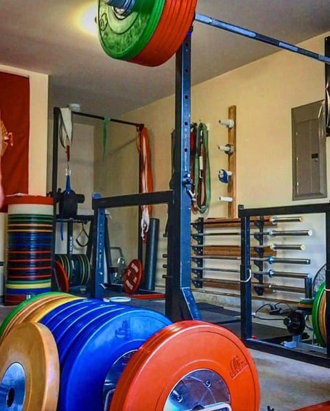 Garage gym with colorful weight plates, barbell storage, and a squat rack setup.