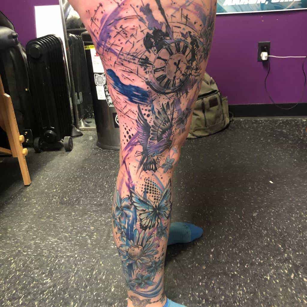 Leg covered in colorful tattoo art featuring a clock, butterflies, and flowers