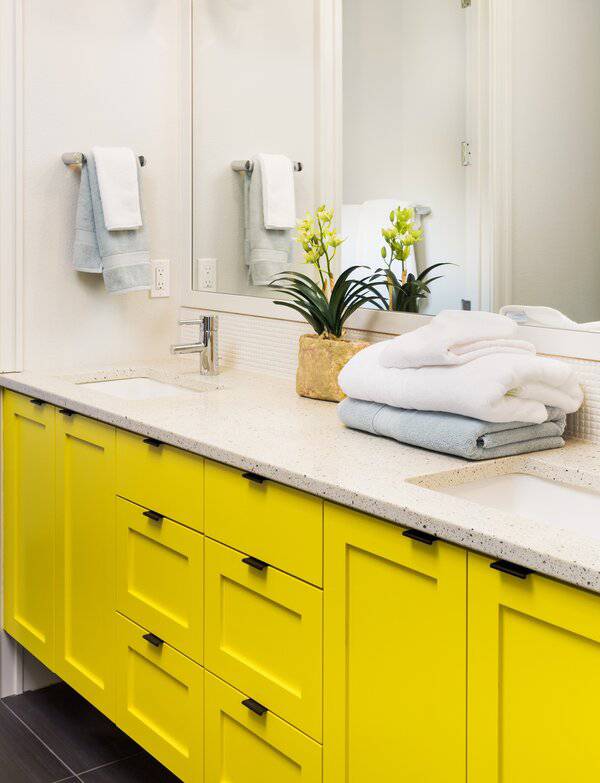 Bathroom featuring yellow cabinets, a white speckled countertop, a small plant, and folded towels for a bright, fresh look.