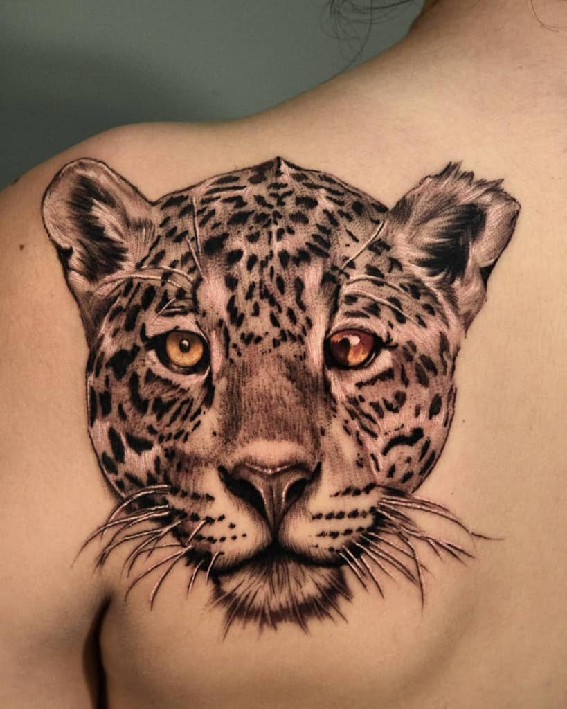 A stunning realistic tattoo of a jaguar's face with captivating eyes, featuring intricate shading and lifelike details, placed on the upper back.