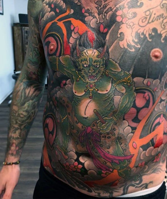 Vibrant Raijin torso tattoo with green thunder god, orange lightning, swirling clouds, and bold Japanese motifs across chest and stomach.