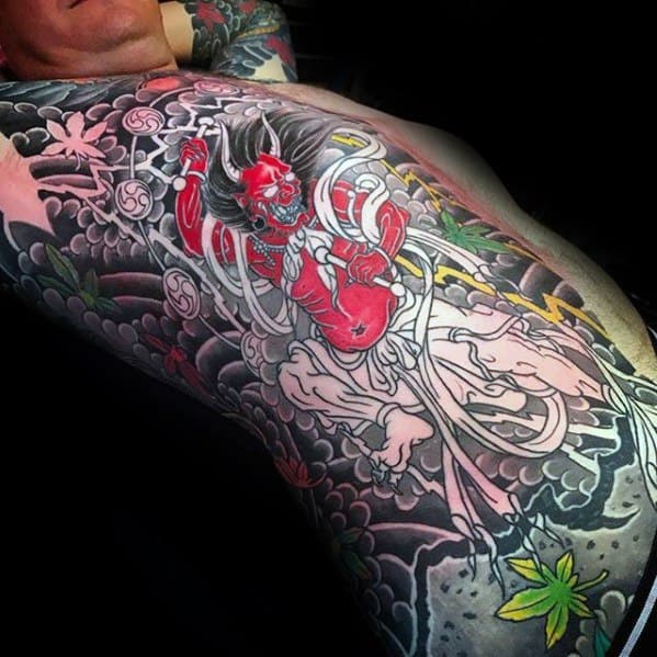 Striking Raijin full torso tattoo with vivid red thunder god, swirling white ribbons, dark storm clouds, and traditional Japanese elements.