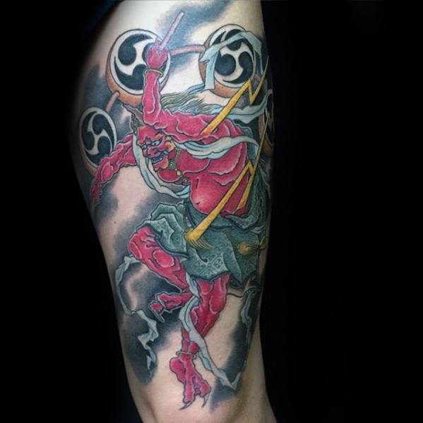 Dynamic Raijin upper arm tattoo with red thunder god, yellow lightning bolts, swirling wind, and black tomoe drums in motion.
