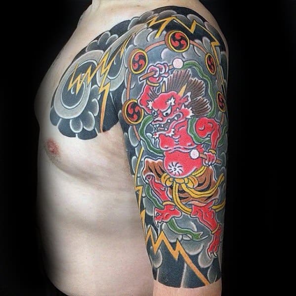 Vivid Raijin upper arm and chest tattoo with red thunder god, swirling clouds, yellow lightning bolts, and traditional tomoe drums.