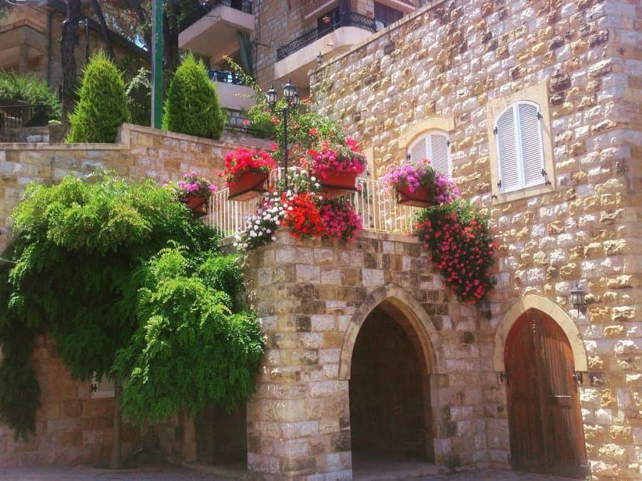 Stone balcony with vibrant railing planters filled with colorful flowers and lush greenery.