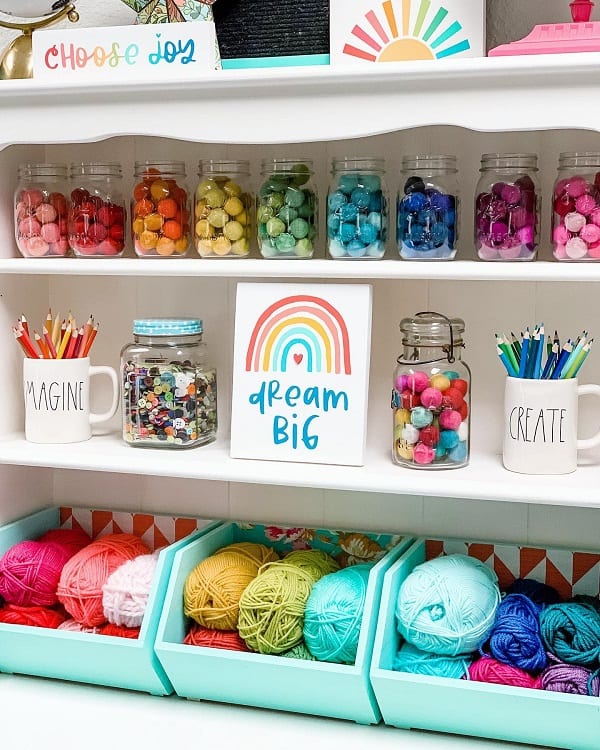 Colorful craft supply shelf with yarn, pom-poms, pencils, and a "Dream Big" sign