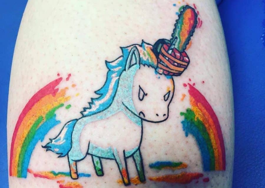 Colorful tattoo of an angry unicorn with a rainbow chainsaw as a horn, set against a vibrant rainbow background with paint splashes.