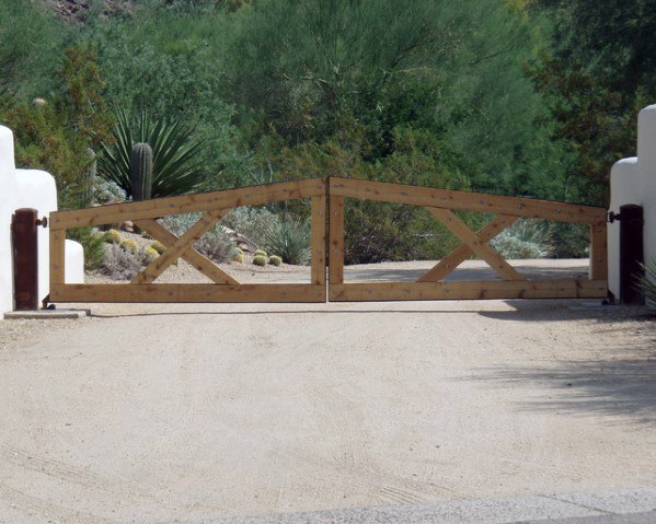 A rustic wooden ranch-style driveway gate with a simple cross-brace design, set against a desert landscape.