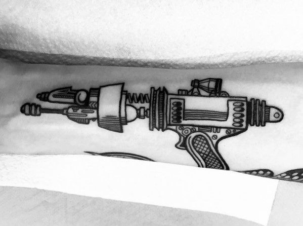 Black and grey ray gun tattoo with intricate linework, futuristic details, and a vintage sci-fi aesthetic for a bold, mechanical look.