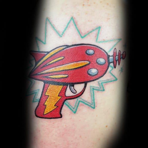 Bold and colorful ray gun tattoo with a classic retro sci-fi design, featuring bright red and yellow tones, a lightning bolt grip, and energy bursts.