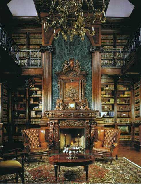Luxurious library with tall bookshelves, ornate fireplace, leather armchairs, wooden table, and a grand chandelier