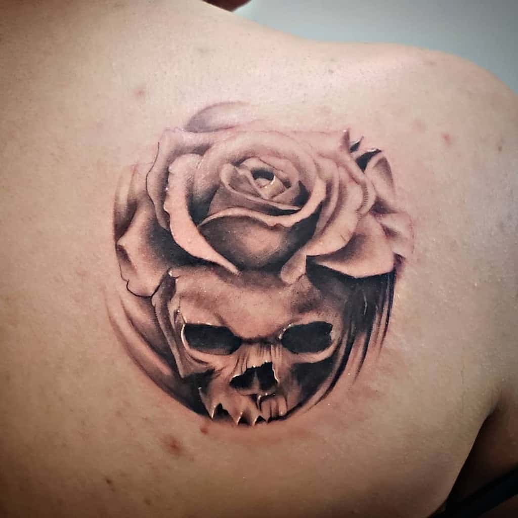 Black and grey back tattoo of a skull seamlessly merging into a blooming rose, featuring soft shading and a surreal design.