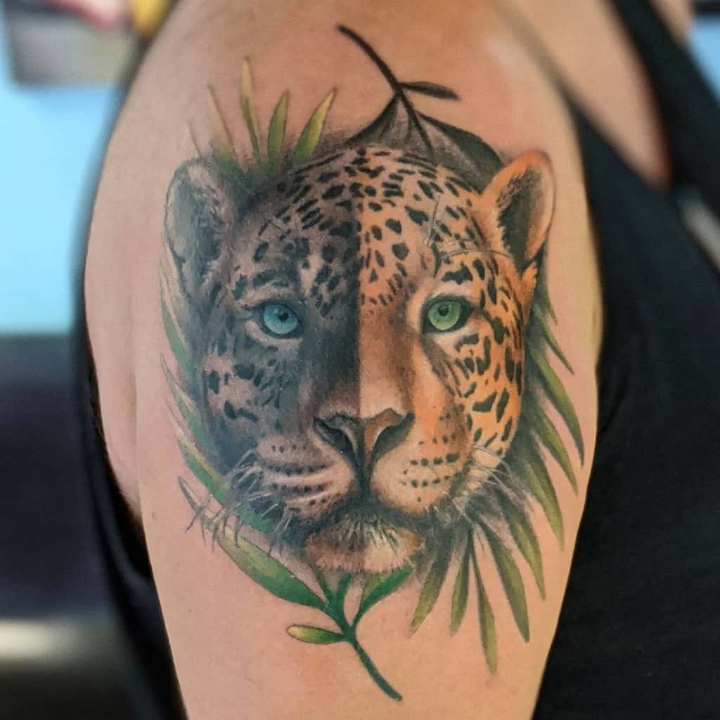 A vibrant tattoo of a jaguar's face, featuring striking blue eyes and surrounded by lush greenery, placed on the upper arm with soft shading and detailed coloring.