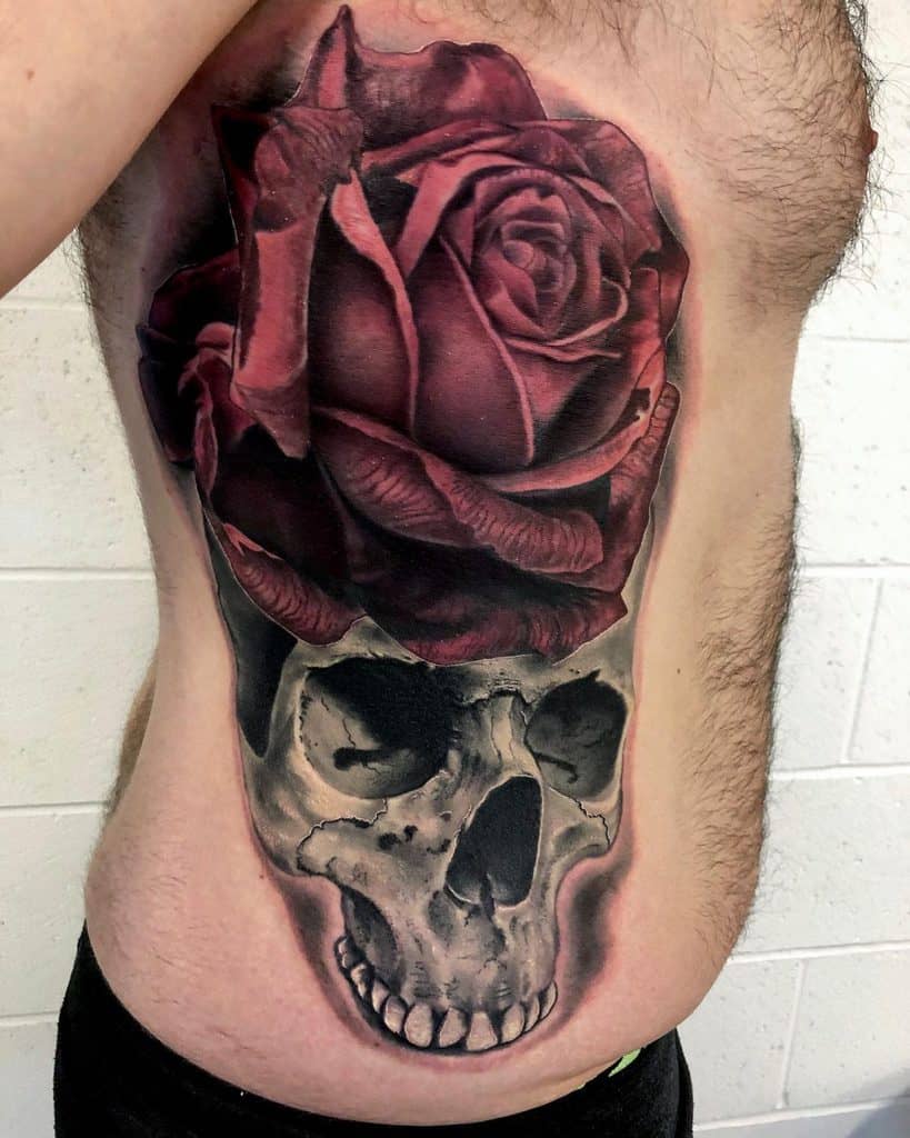 Tattoo of a red rose above a skull on a man's side