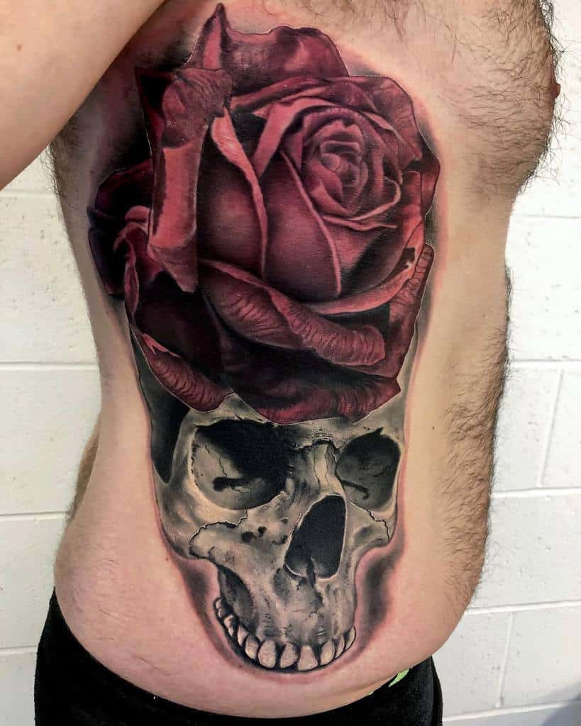 Realistic ribcage tattoo of a detailed skull with a large, deep red rose, blending dark and vibrant elements for a bold design.