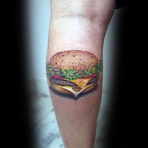 A tattoo of a juicy cheeseburger with lettuce and tomato on someone's leg