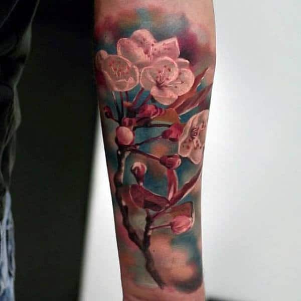 Forearm tattoo of realistic cherry blossoms with pink petals and buds on a blue and green watercolor background