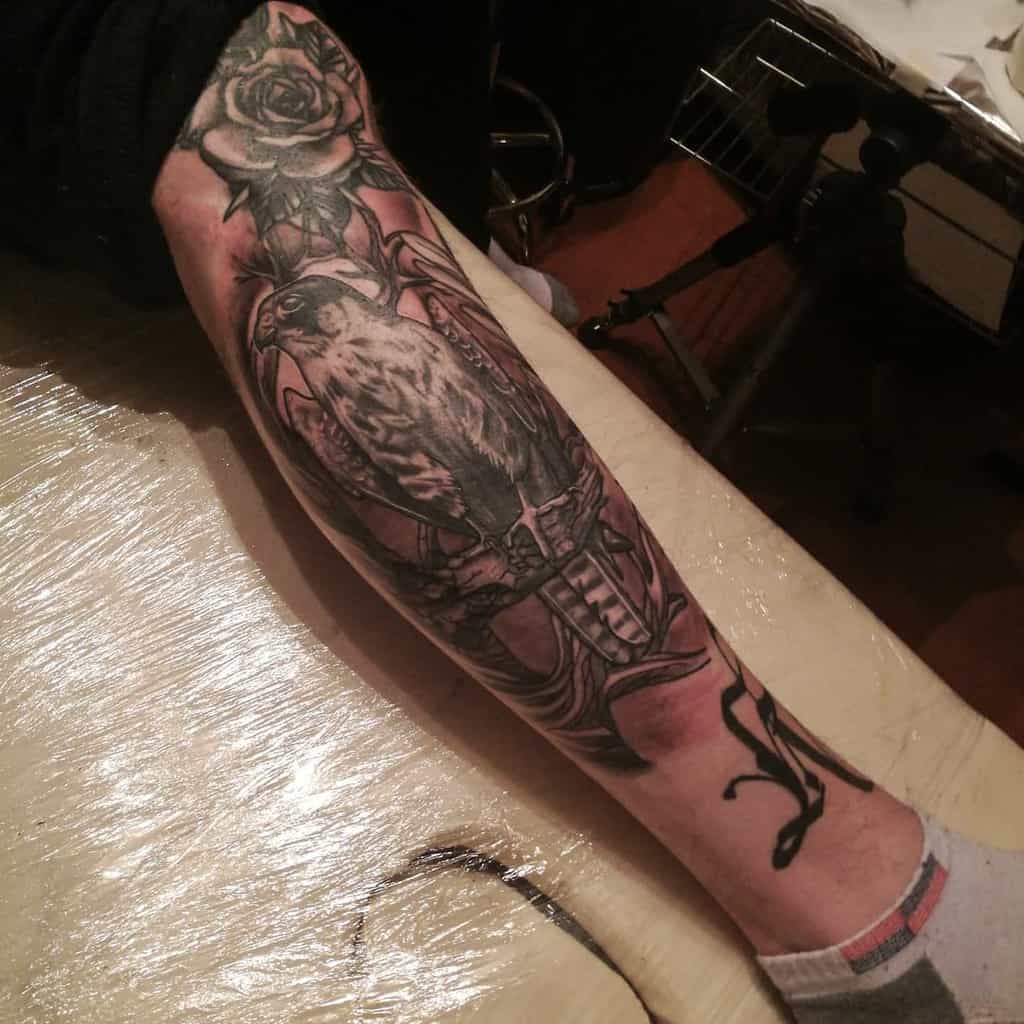 Detailed black and gray leg sleeve tattoo featuring a rose, a falcon perched on a branch, and abstract designs
