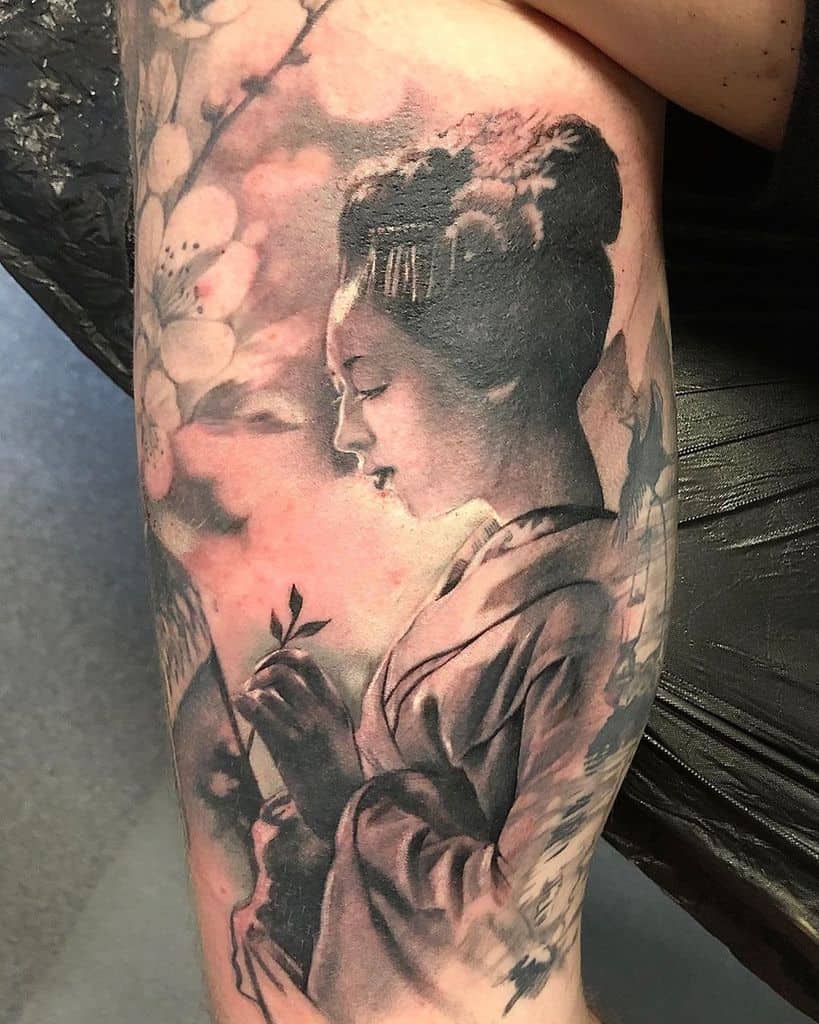 Realistic black and gray tattoo of a Geisha in a serene pose, holding a branch, surrounded by soft cherry blossoms and delicate shading.