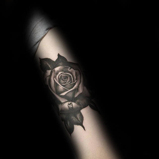 A black and gray rose tattoo on a forearm