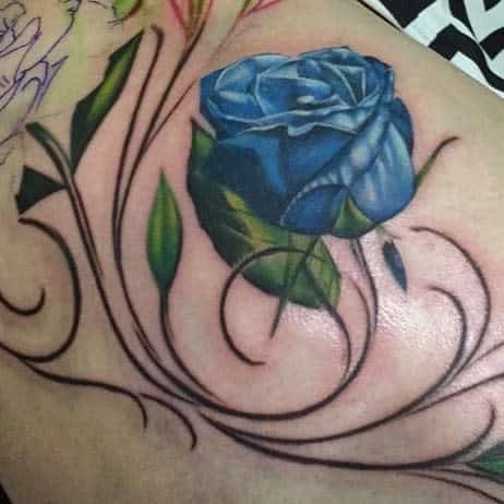 A mesmerizing blue rose tattoo elegantly entwined with swirling vines and vibrant green leaves