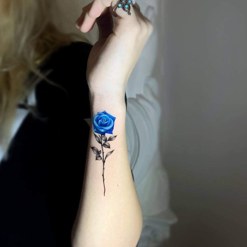 A realistic blue rose tattoo on the forearm, featuring detailed petals and stems in black and grey ink