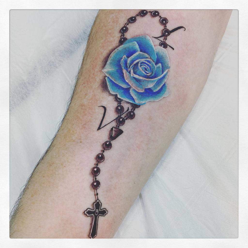 A striking tattoo featuring a delicate blue rose intertwined with a rosary and cross adorns the arm
