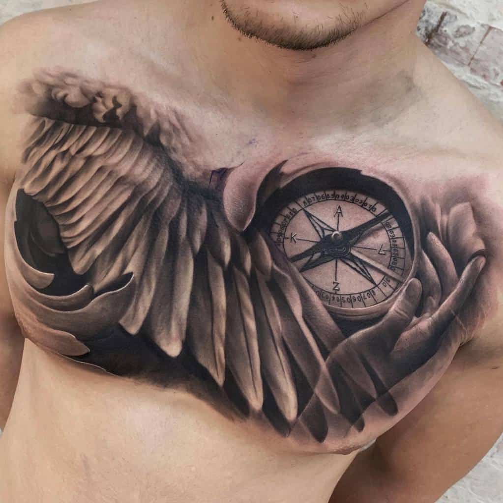 A tattoo featuring realistic angel wings and a hand holding a detailed compass