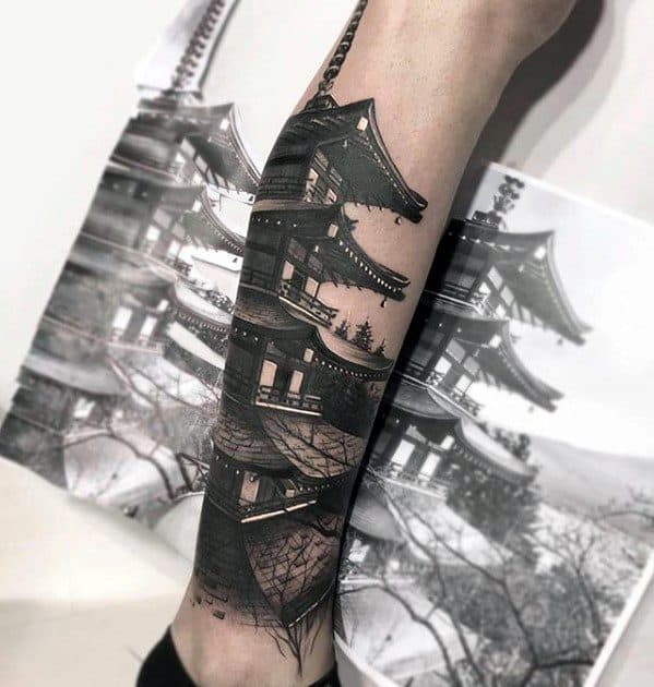 Hyper-realistic black and grey forearm tattoo of a Japanese pagoda with sharp architectural detail, layered shading, and bare tree branches.