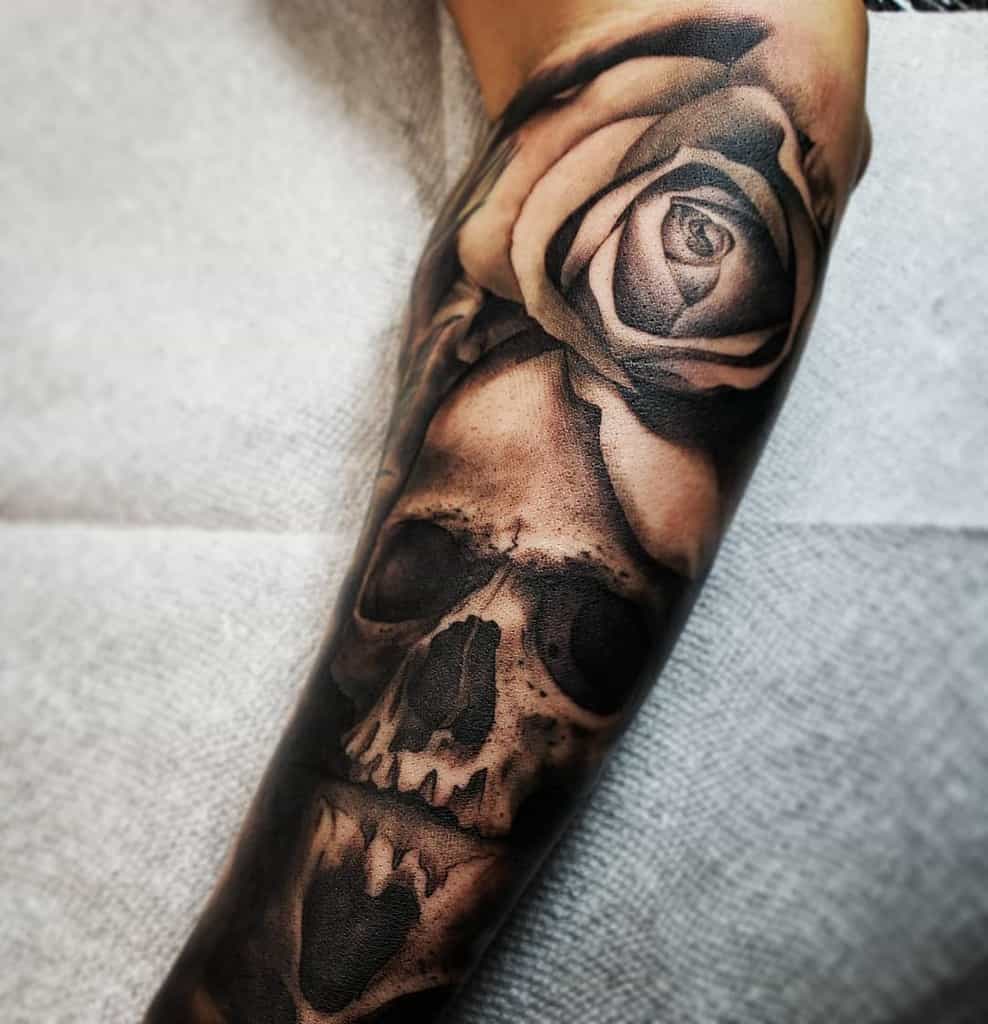 Black and grey forearm tattoo of a realistic skull with a detailed rose, featuring smooth shading and high contrast for a dramatic effect.