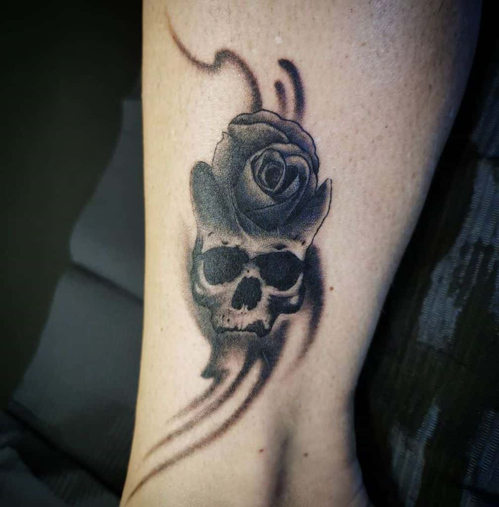 Black and grey tattoo of a skull seamlessly blending into a blooming rose, with soft shading and flowing smoke-like details.