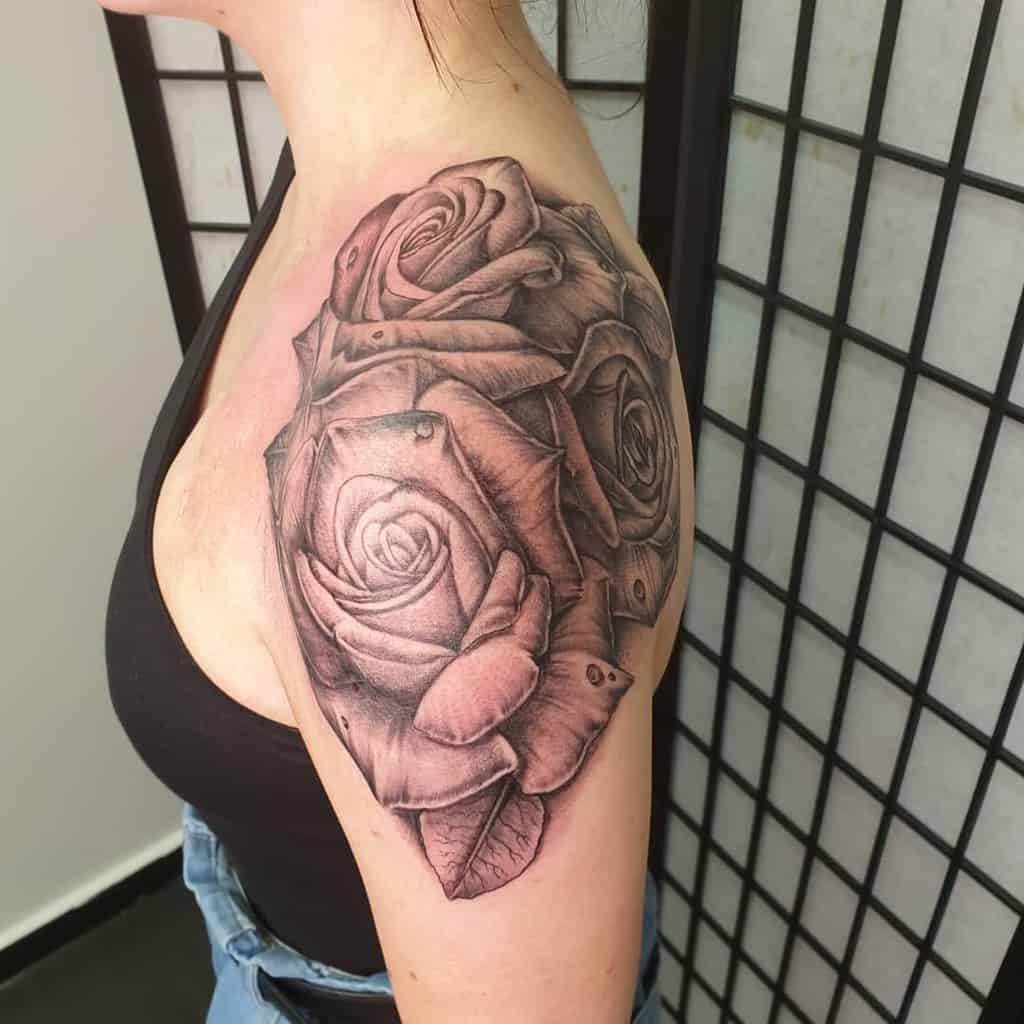 A stunning arm and shoulder tattoo showcases detailed black and gray roses with intricate shading